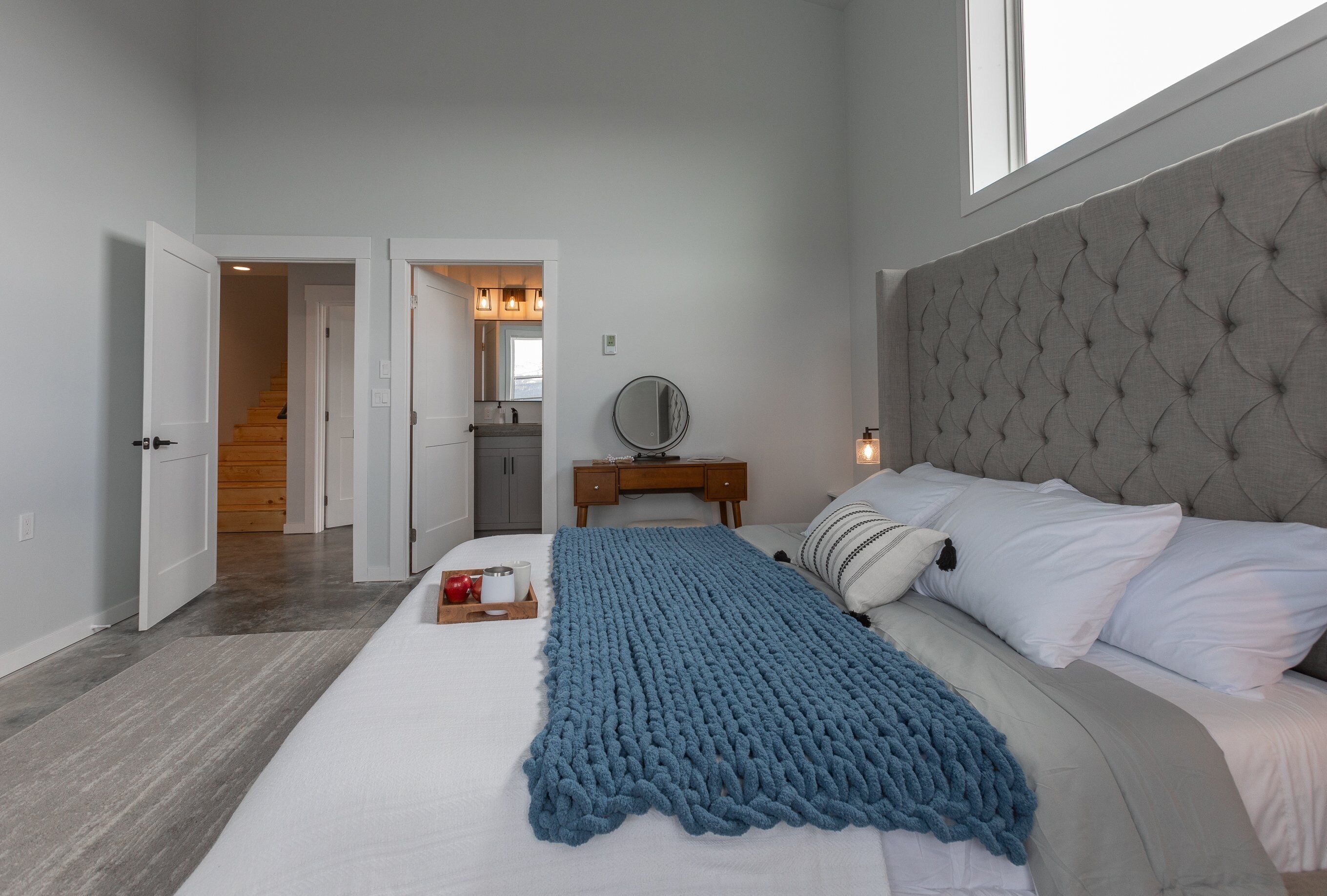 A bedroom with a bed, a bedside table, a mirror, and a window.
