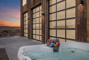 A hot tub with a colorful towel, wooden exterior walls, and large windows. - Camp Nash (Island Park)