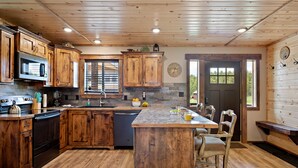A kitchen with wooden cabinets, a central island, and a stone backsplash. - Set the Hook (Island Park)