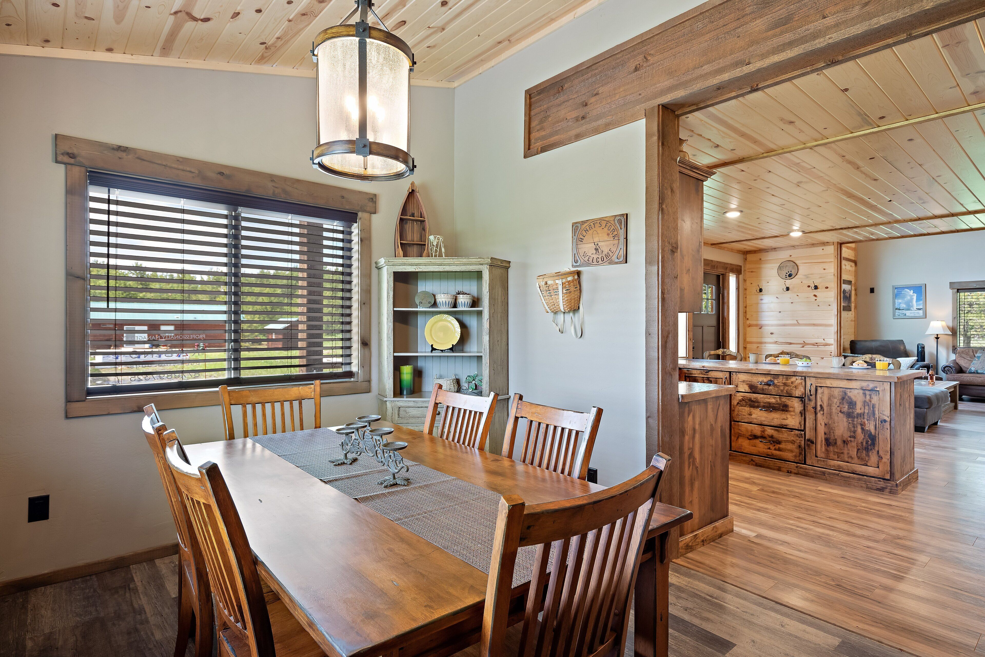 Un comedor con mesa y sillas de madera, techo de madera y vista a la cocina al fondo.