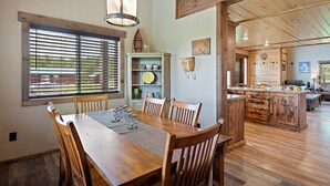 A dining area with a wooden table and chairs, a wooden ceiling, and a view of the kitchen in the background. - Set the Hook (Island Park)