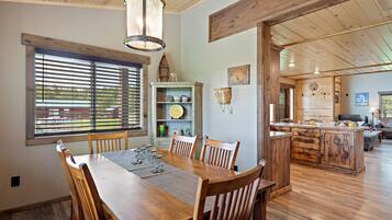 Un comedor con mesa y sillas de madera, techo de madera y vista a la cocina al fondo.