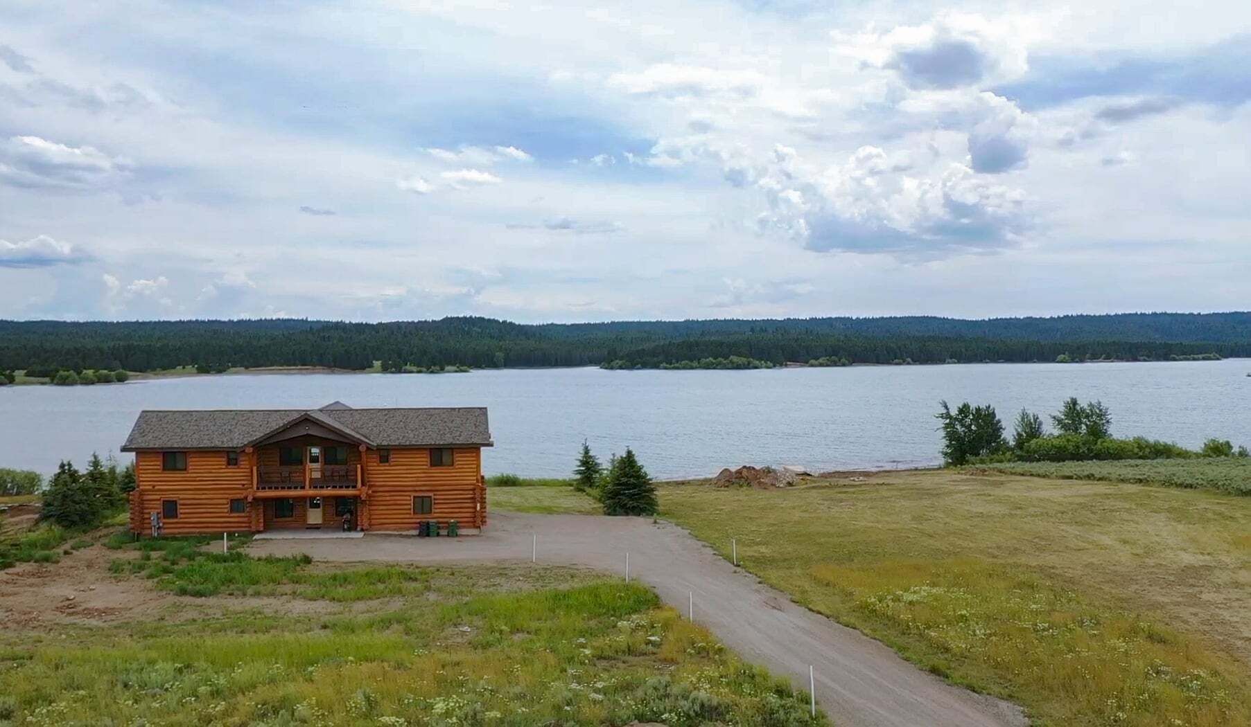 Une cabane en rondins avec un porche, une allée et une vue sur le lac.