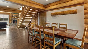 Ein Esszimmer mit Holzboden, einem großen Tisch und Stühlen, einer Holztreppe und einem Kamin.