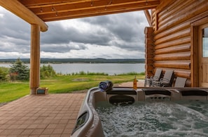 Un bain à remous avec vue sur un lac, une terrasse en bois et des sièges d’extérieur.
