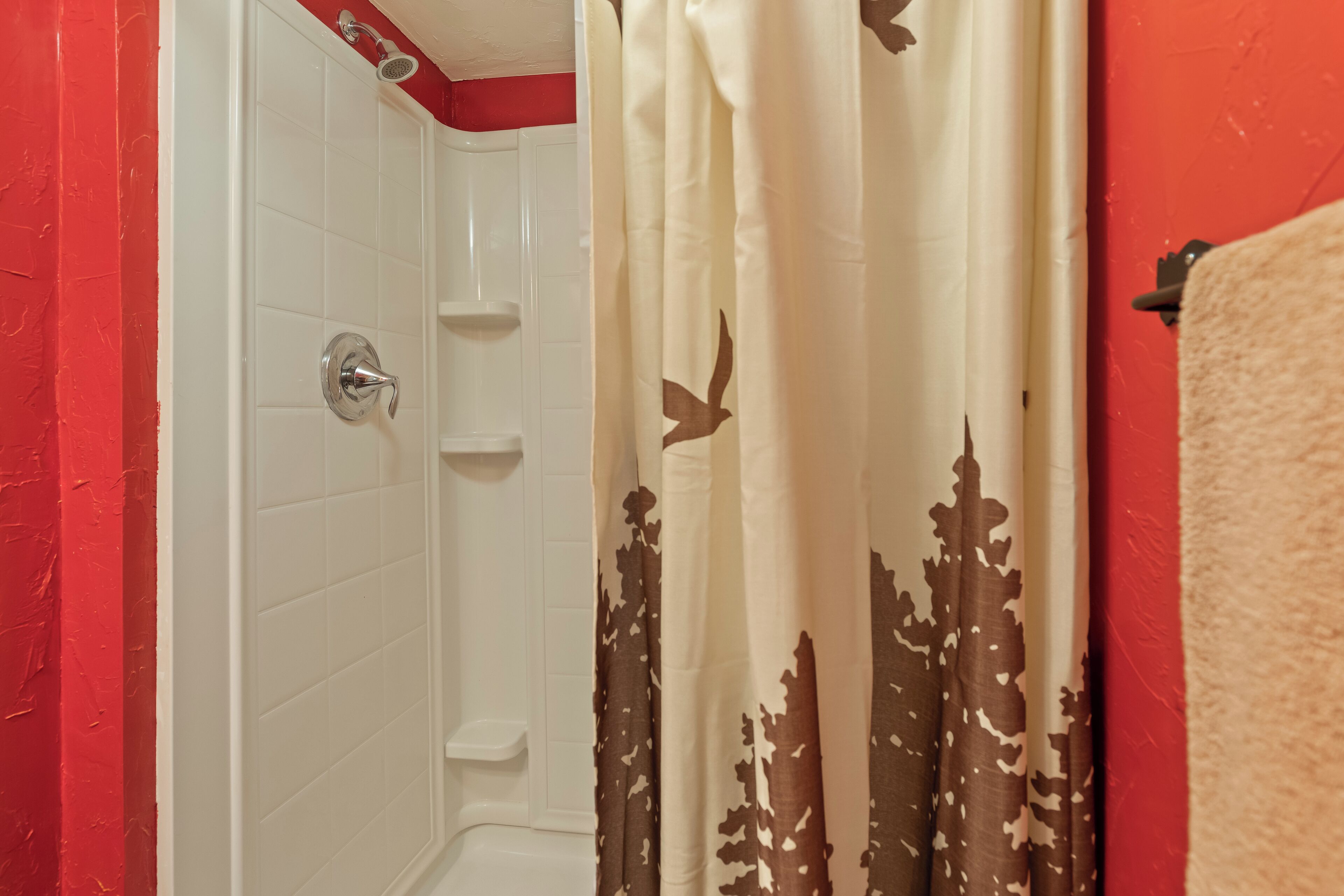 Une salle de bain avec une douche, des murs recouverts de carreaux blancs et un mur d’accent rouge.