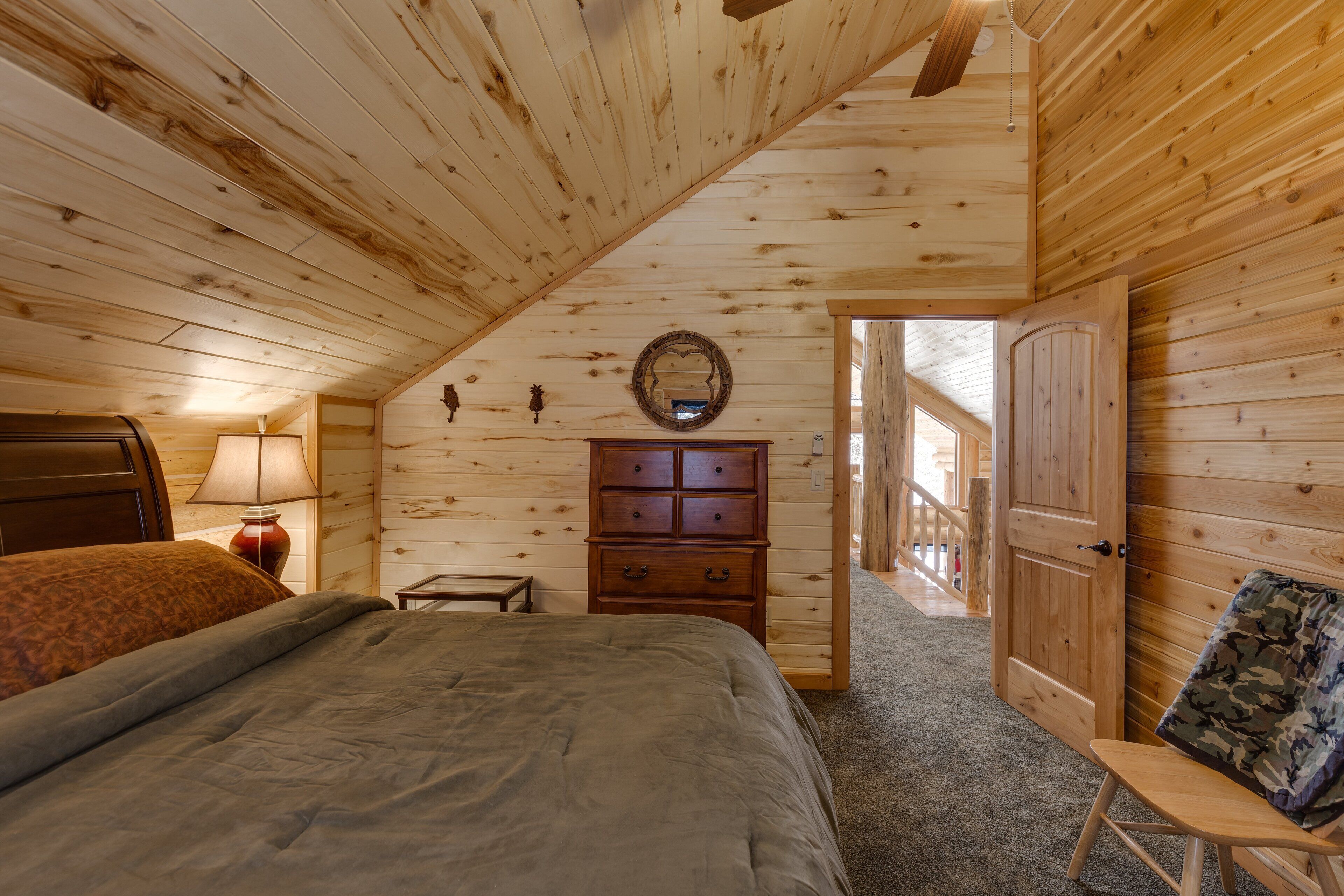 A bedroom with a wooden ceiling, a bed, a dresser, and a door leading outside.