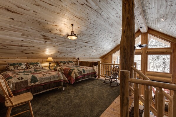 A cozy log cabin bedroom with two beds, a rocking chair, and a large window. - Lumberjack Lodge (Island Park)
