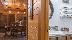 A wooden interior with a dining area, wooden walls, a kitchen, and a bathroom with a sink and towel rack. - Deer View (Island Park)