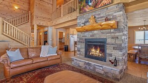 Ein geräumiges Wohnzimmer mit Kamin aus Stein, einer Ledersofa und einer Treppe, die in einen oberen Bereich führt.