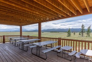 A covered outdoor area with picnic tables and a view of a grassy field and mountains. - Liberty Lodge (Island Park)