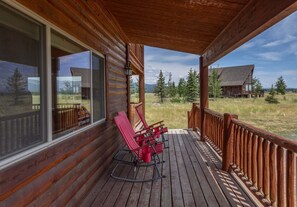 A wooden porch with rocking chairs and a view of a mountain landscape. - Liberty Lodge (Island Park)