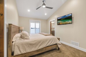 A bedroom with a wooden bed, a ceiling fan, a large window, and a television on the wall. - Kings Retreat (Island Park)