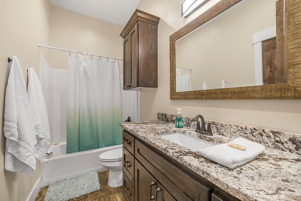 A bathroom with a bathtub, toilet, and vanity with a sink and mirror. - Kings Retreat (Island Park)