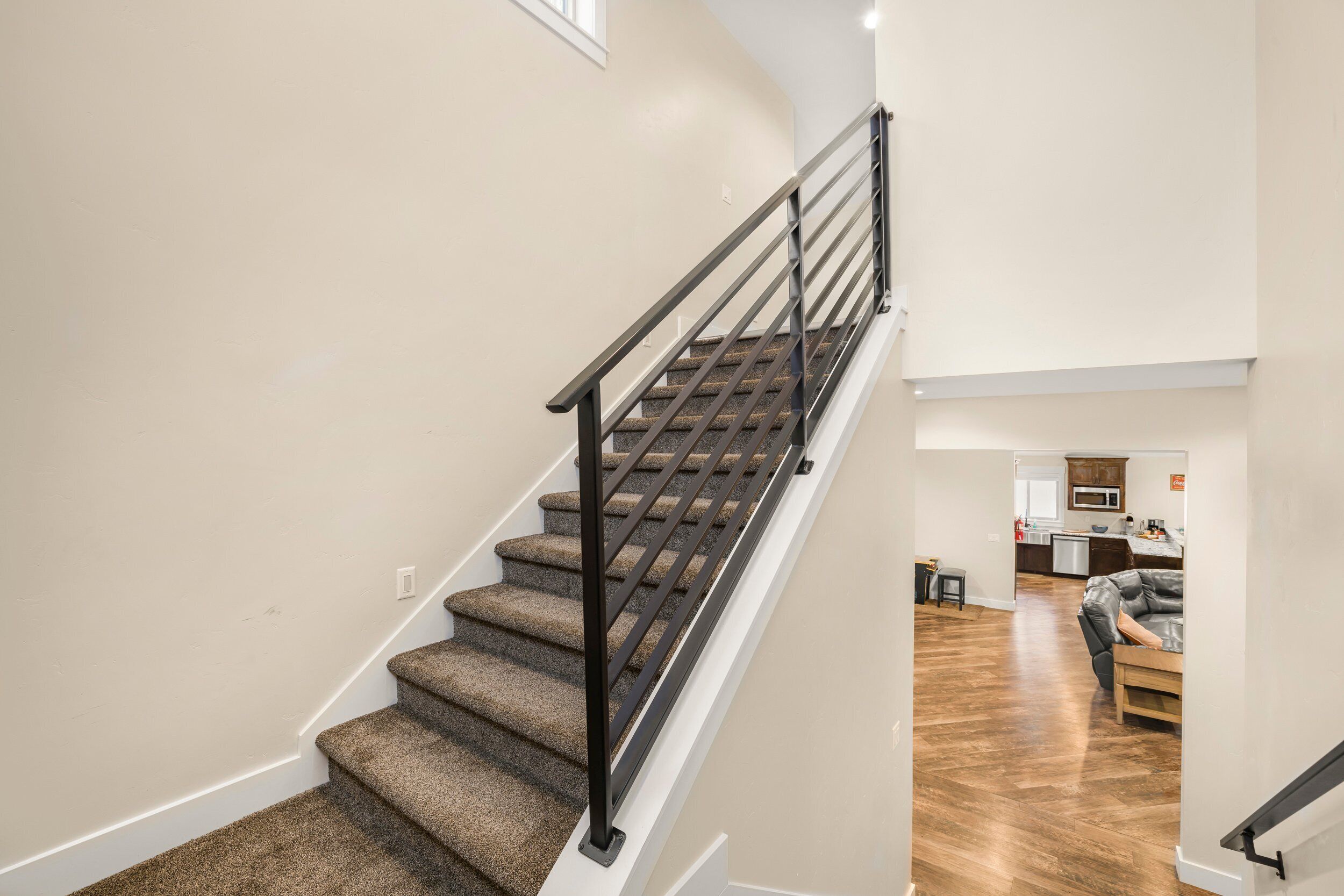 A staircase with carpeted steps and a metal railing leading to a living area with a wooden floor and a gray sofa.