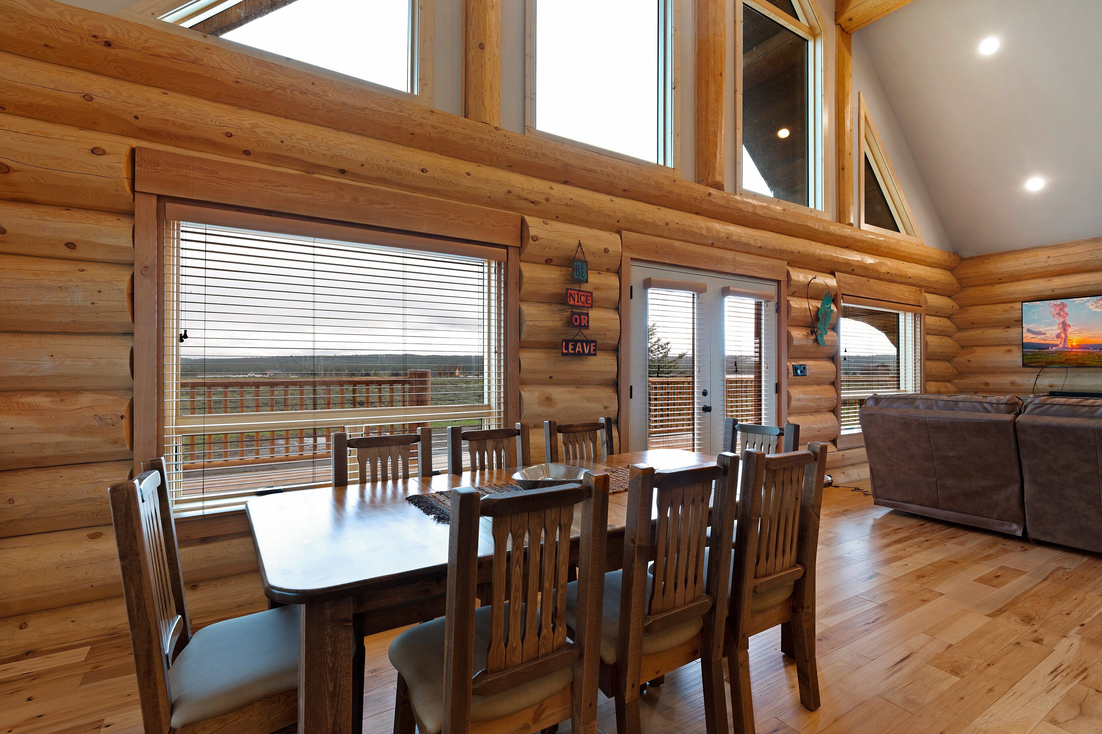 A log cabin interior with a dining area, wooden walls, and large windows.
