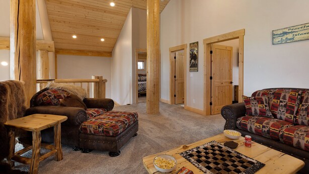 Ein gemütliches Wohnzimmer mit Holzboden, einer Couch, einem Sessel, einem kleinen Tisch und einem Schachbrett.