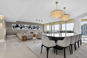 A modern living room with a large round table, white chairs, and a large abstract painting on the wall. - Coastal Enclave Key Biscayne Oceanview w Pool (Key Biscayne)