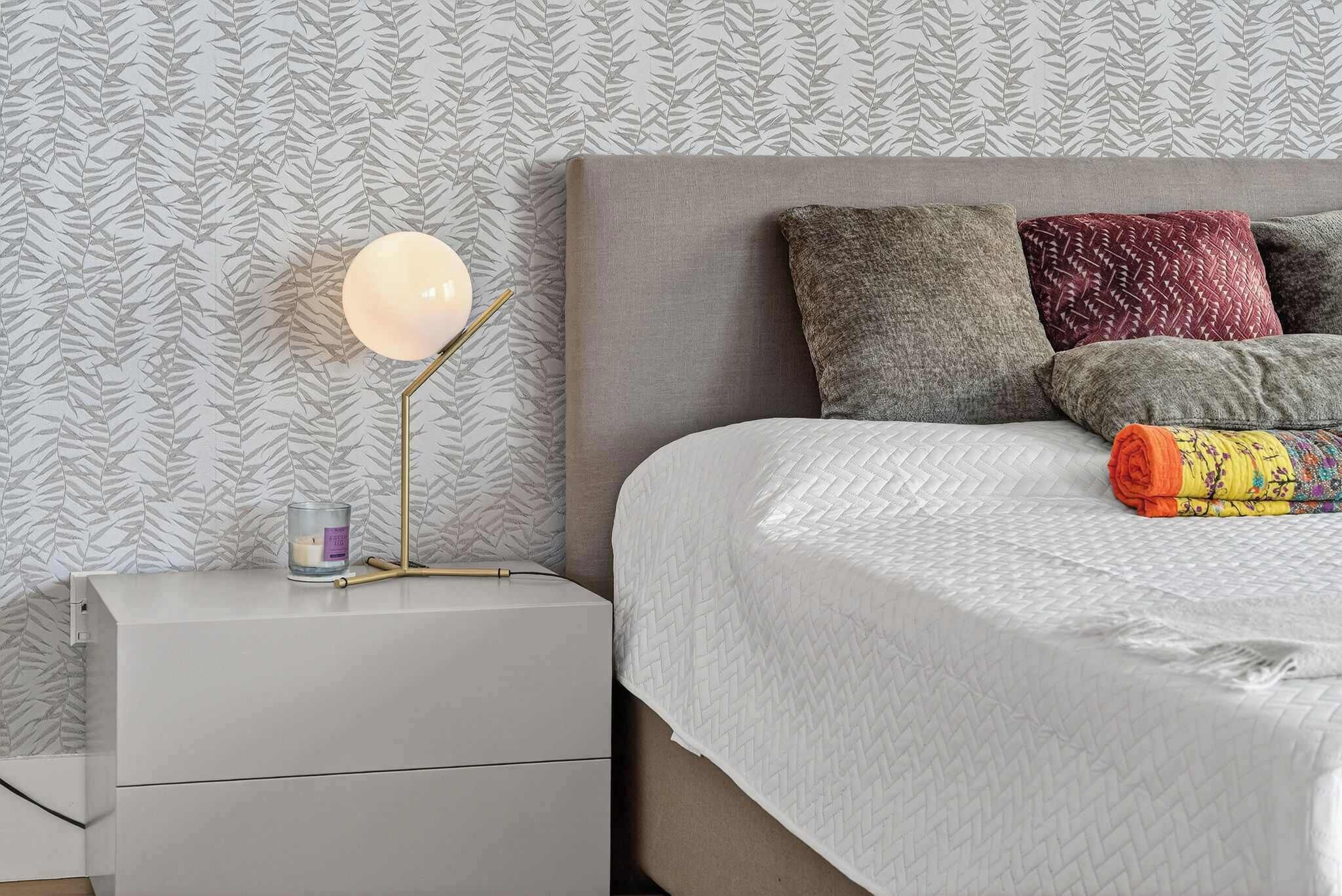 A neatly made bed with a white quilt, a bedside lamp, and a nightstand with a candle and a book.