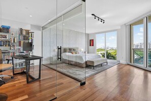 A modern bedroom with a glass partition, a large bed, a desk, and a bookshelf. - Coastal Enclave Key Biscayne Oceanview w Pool (Key Biscayne)