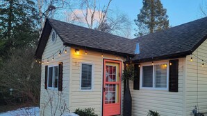 Una pequeña casa de un piso con una puerta roja, una chimenea y un camino de piedra que conduce a la entrada.
