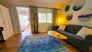 Una sala de estar con un sofá, una mesa de centro y una alfombra. Hay una ventana con cortinas, una puerta y una pared decorada con una obra de arte circular.