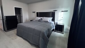 Een slaapkamer met een groot bed, een nachtkastje, een televisie en een raam met gordijnen.