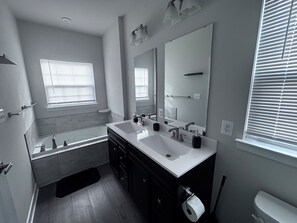 A modern bathroom with a bathtub, two sinks, a large mirror, and a toilet.
