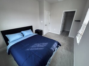 A bedroom with a large bed, a nightstand, a door, and a window.