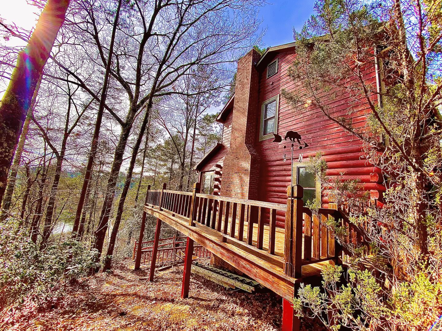 Une cabane rustique en rondins de bois, dotée d’une terrasse en bois et d’une cheminée, entourée d’arbres.