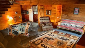 A log cabin interior with a sofa, armchair, and bed with patterned bedding. - Moonlit Mountain: A peaceful escape to reconnect, unwind, and breathe deep (Ellijay)