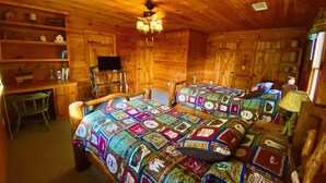 A cozy cabin room with wooden walls and ceiling, two beds with colorful quilts, a desk with a chair, and a television on a shelf. - Moonlit Mountain: A peaceful escape to reconnect, unwind, and breathe deep (Ellijay)
