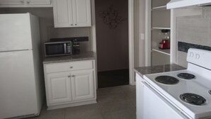 Una cocina con armarios blancos, un microondas, una estufa y un refrigerador.