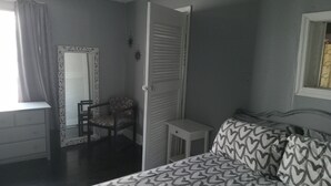 Un dormitorio con cama, una silla, una mesita y una ventana con cortinas.