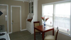 Comedor con mesa y sillas de madera, un florero con flores, una ventana con persianas y un ventilador de techo.
