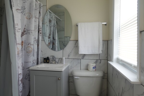 A bathroom with a white sink, mirror, toilet, and shower curtain with text patterns. - Freedom Inn Motel (Grantville)