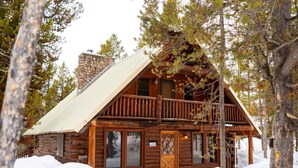 Una cabaña rústica de troncos con balcón, rodeada de nieve y árboles.