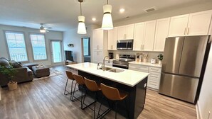 A modern kitchen with white cabinets, stainless steel appliances, and a central island with bar stools. - Luxurious 2 Bed 2 Bath • Pool • Gym • Game Room (Waukee)