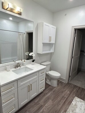A bathroom with a white vanity, a sink, a mirror, a toilet, and a cabinet above the toilet. - Luxurious 2 Bed 2 Bath • Gym • Pickleball Courts • Game Room (Waukee)