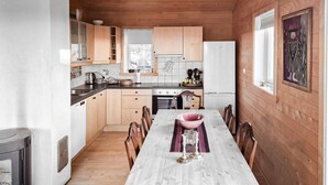 Een kleine keuken met houten kastjes, een eettafel met stoelen en een koelkast.