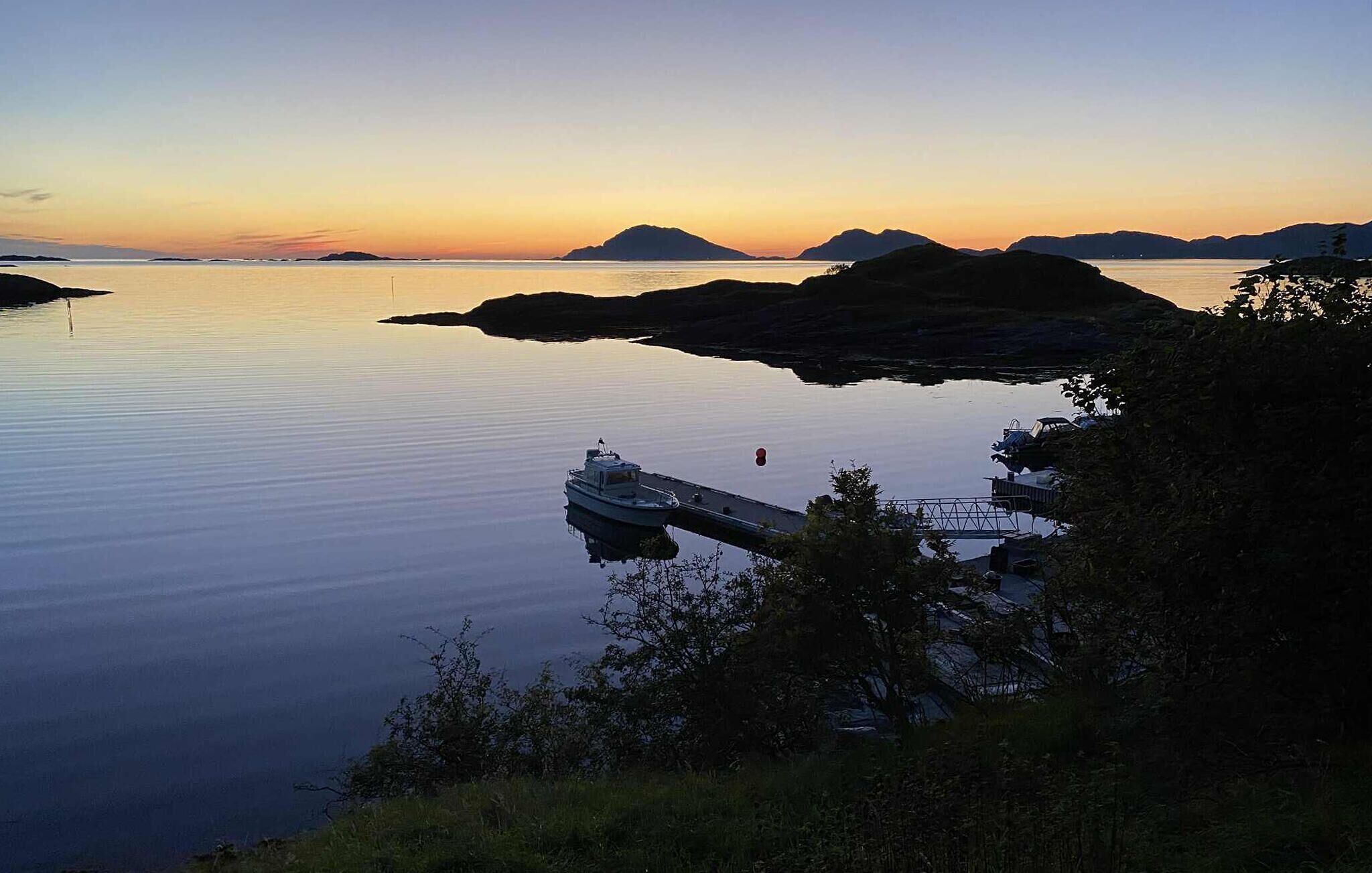 A calm body of water with a dock and a boat, surrounded by hills and trees.