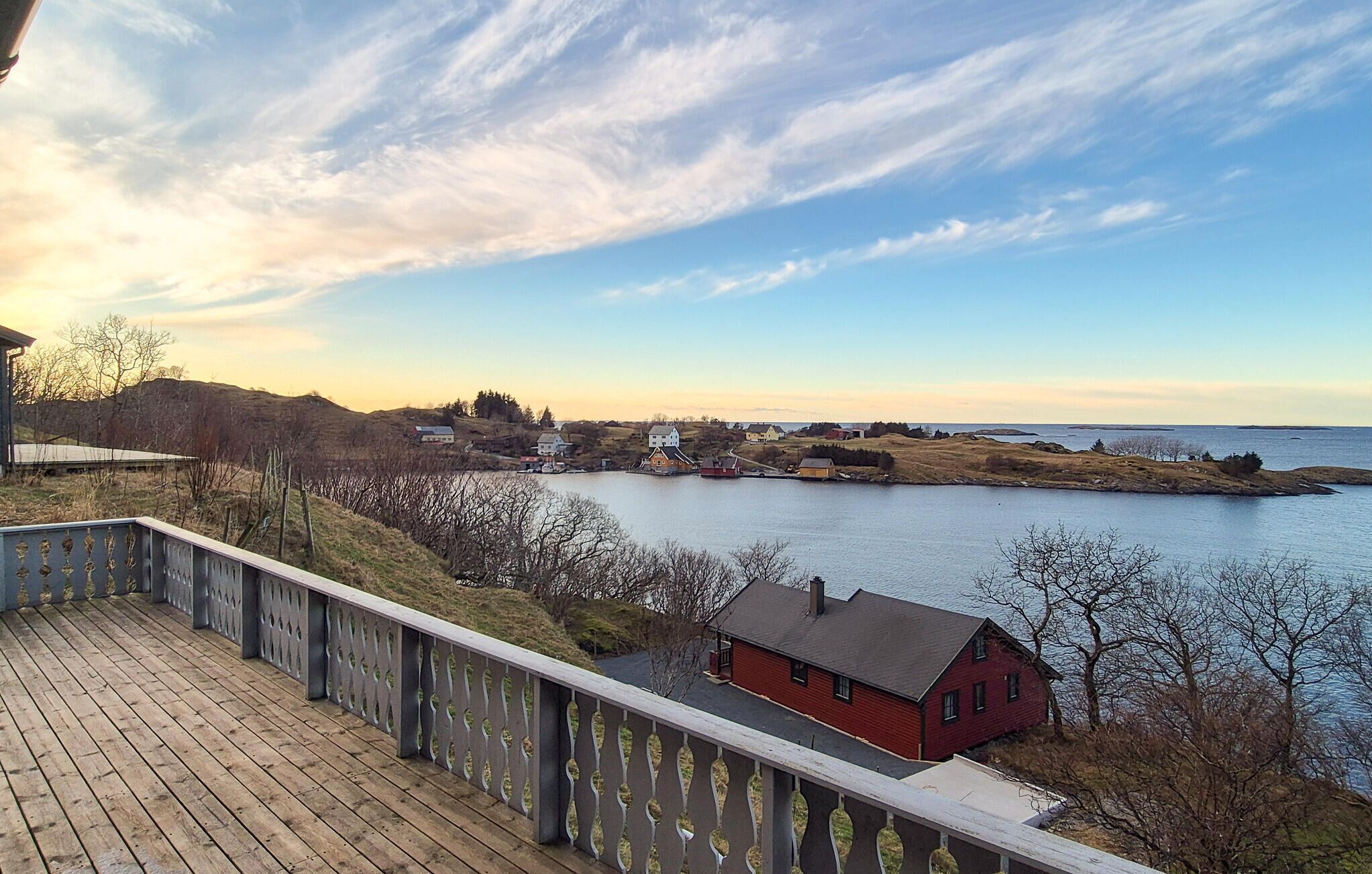 A wooden deck with a railing overlooking a body of water and a small red house.