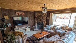Un salon chaleureux, aménagé dans le style d’un chalet, avec une cheminée en pierre, un téléviseur et un canapé.