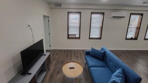 Een moderne woonkamer met een flatscreen-tv, een blauwe bank, een ronde houten salontafel en een schuifdeur.