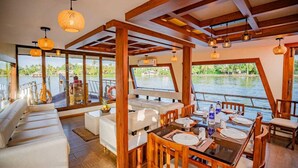 A boat interior with a dining area, white sofas, and a view of the water. - Riverine Kadavil Houseboat (Alappuzha)