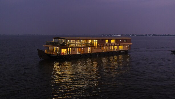 A large, multi-level houseboat with multiple decks and balconies, floating on calm water at dusk. - Riverine Kadavil Houseboat (Alappuzha)