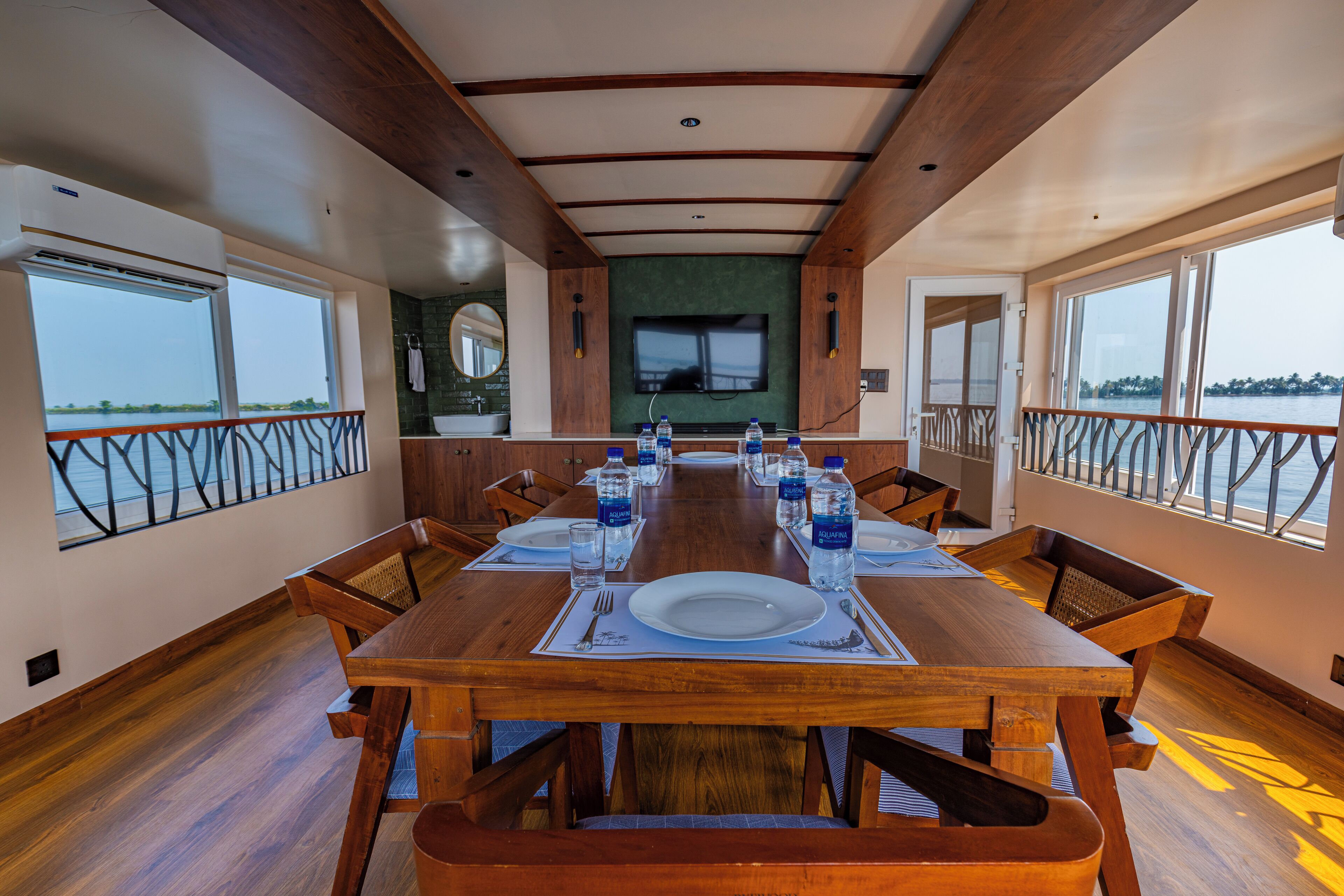 A dining area with a long wooden table set for six, equipped with water bottles, plates, and cutlery.
