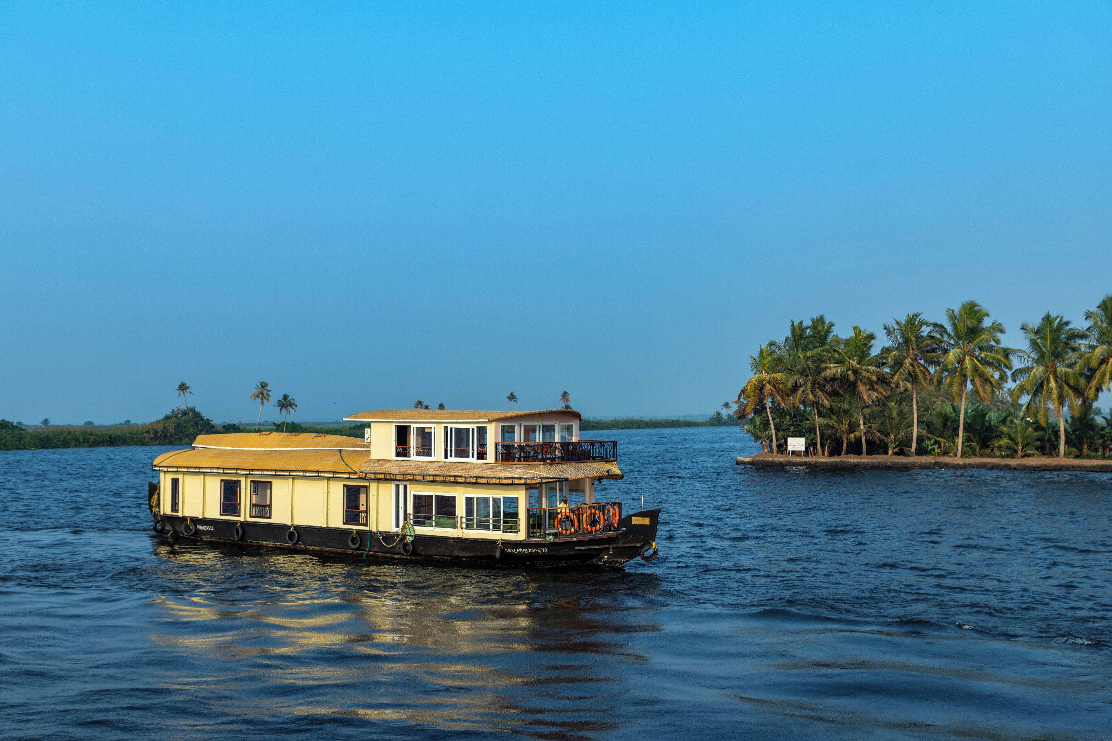 A houseboat with a two-story structure, large windows, and a balcony on the upper deck.
