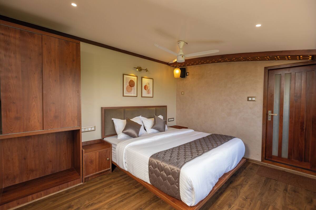 Une chambre d’hôtel avec un grand lit, une armoire en bois, un ventilateur de plafond et un luminaire fixé au mur.