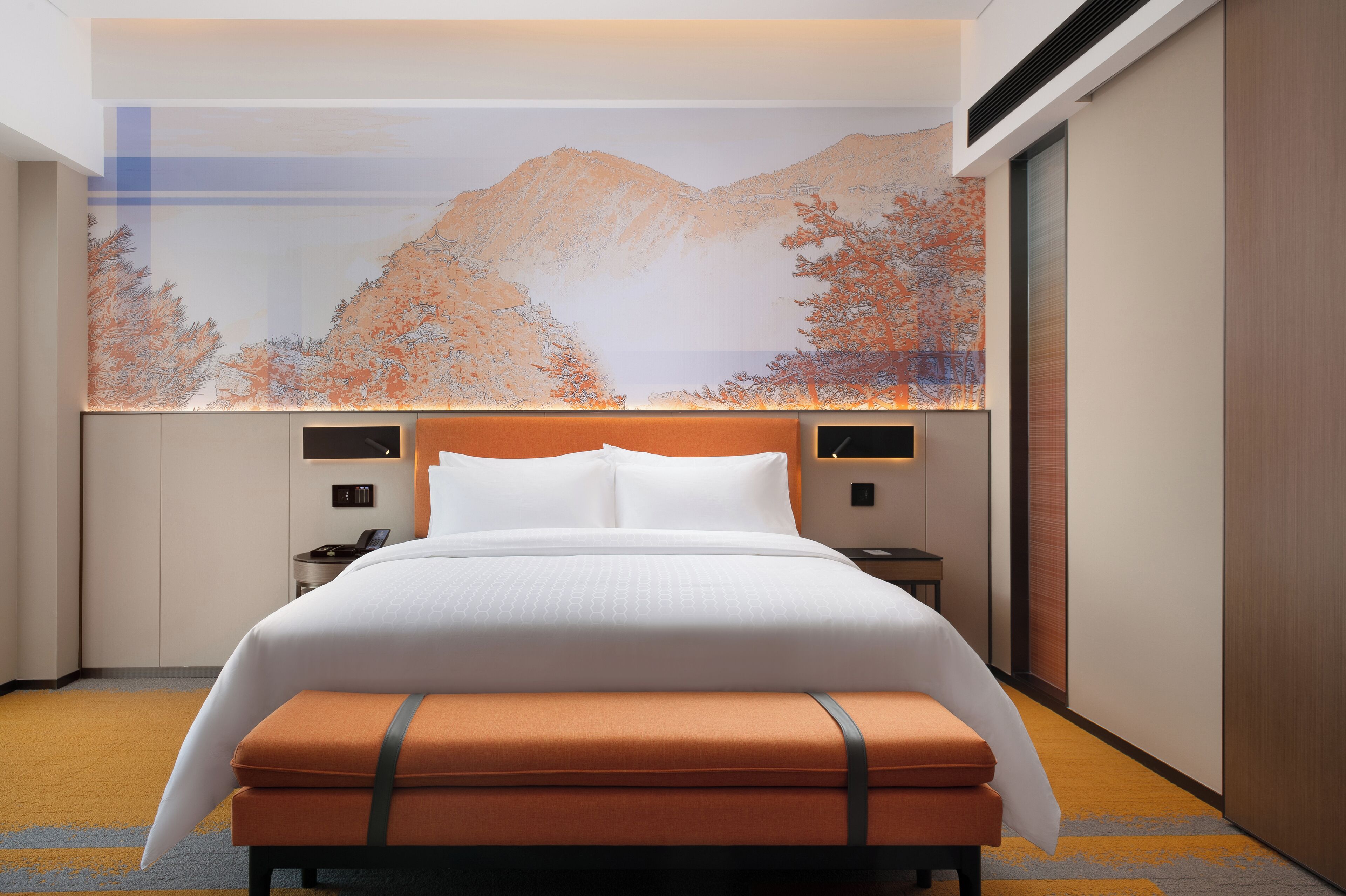 A hotel room with a large bed, a nightstand, a wall-mounted TV, and a large window with a mountain view.